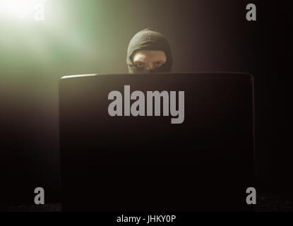 Angry business man as computer hacker in suit stealing data from laptop in front of black background Stock Photo
