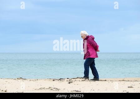 A senior woman walking on on the shoreline of a sandy beach in Dornoch, Sutherland, Scotland, UK Stock Photo