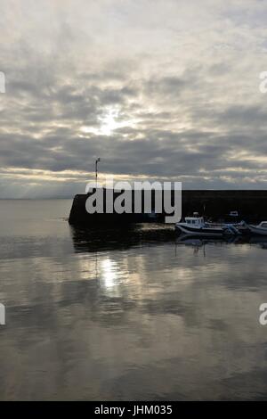 Calm sea reflections with little boats sheltering behind the pier at the quiet village of Portmahomack in Easter Ross, Scotland, UK Stock Photo