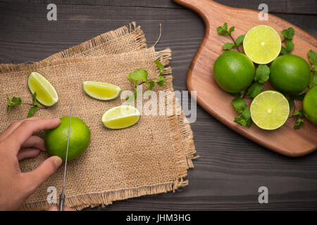 Fresh limes on cutting board on wooden table. Top view, background. Stock Photo