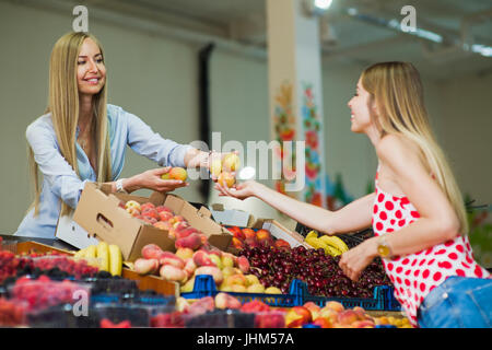 A woman buys fruits in the market. Woman seller is holding peaches in her hands. Focus on hand.. Stock Photo