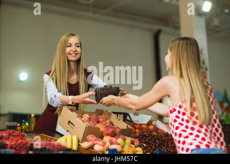 A woman buys berries in the market. Woman seller is holding blueberries in her hands. Focus on berries. Stock Photo