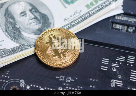 Close up shot gold Bitcoin on dollar banknote over computer print circuit board shallow depth of field Stock Photo