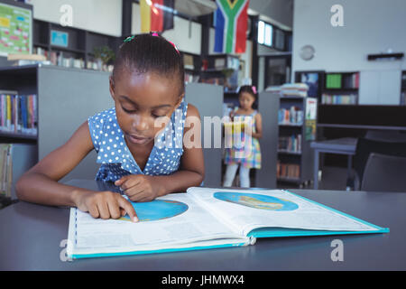 Girl reading book at desk in library Stock Photo