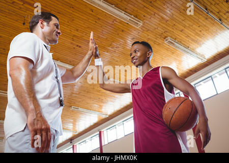 Low angle view of basketball player high fiving with coach while standing in court Stock Photo