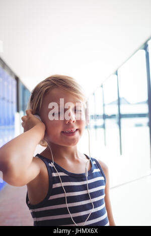Elementary girl with eyes closed listening music through headphones while standing in corridor at school Stock Photo