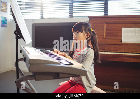 Concentrated girl looking at notes while practicing piano in music class Stock Photo