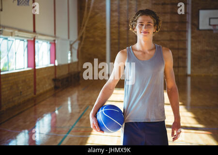 Portrait of smiling young man with basketball standing on hardwood floor in court Stock Photo