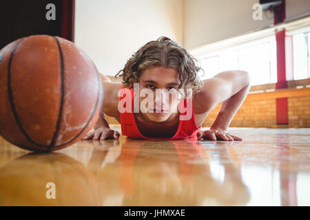 Portrait of male basketball player exercising by ball on hardwood floor in court Stock Photo