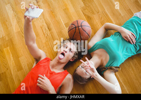 Overhead view of friends taking selfie while lying on hardwood floor in court Stock Photo
