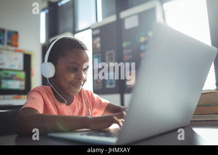 Boy listening music while using laptop at desk in school Stock Photo
