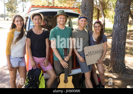 Portrait of friends with sign board standing by camper van on field Stock Photo