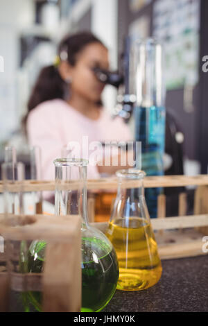 Flasks of chemicals on desk with elementary student using microscope in background at science laboratory Stock Photo