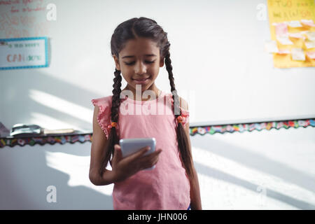 Girl using mobile phone while standing against wall in school Stock Photo