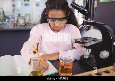 Elementary student writing in book by microscope on desk at science laboratory Stock Photo