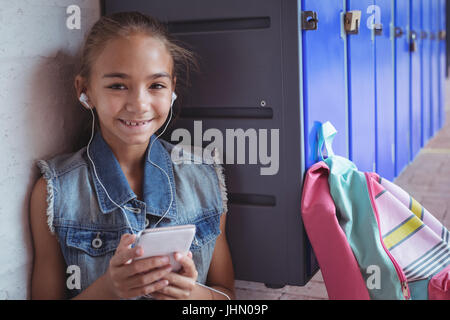 Portrait of elementary schoolgirl listening music through headphones by lockers at school Stock Photo