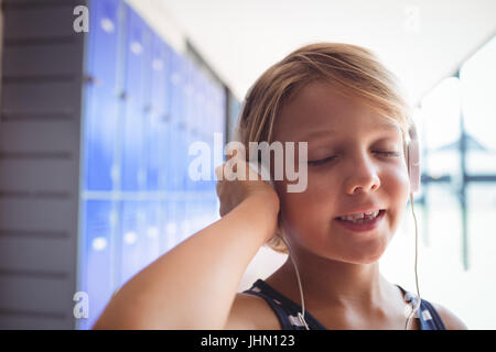 Elementary student with eyes closed listening music through headphones while standing in corridor at school Stock Photo