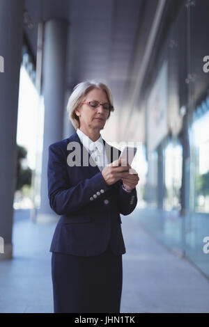 Businesswoman using smart phone while standing on sidewalk Stock Photo