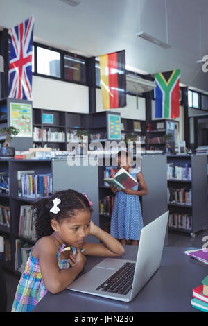 Concentrated girl looking at laptop while sitting at desk in library Stock Photo