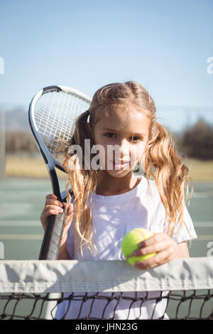 Portrait of girl holding racket and tennis ball at court on sunny day Stock Photo