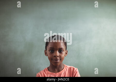 Portrait of smiling boy against blank greenboard in classroom Stock Photo