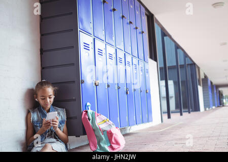 Elementary schoolgirl listening music through headphones while using mobile phone by lockers at school Stock Photo
