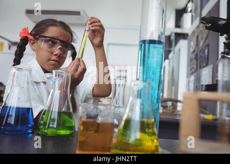 Elementary student examining yellow chemical in test tube by desk at science laboratory Stock Photo