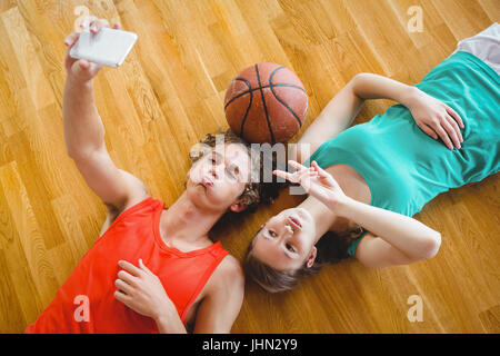 Overhead view of playful friends taking selfie while lying on hardwood floor in court Stock Photo