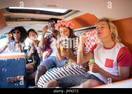 Happy friends blowing bubble wands while sitting in camper van Stock Photo