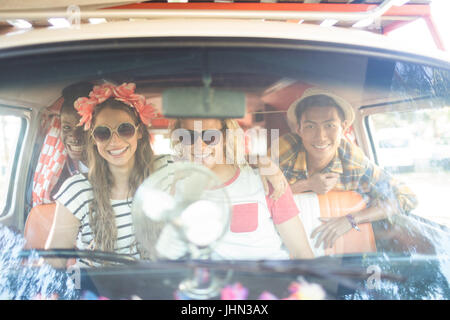 Portrait of happy friends sitting together in camper van seen through windshield Stock Photo