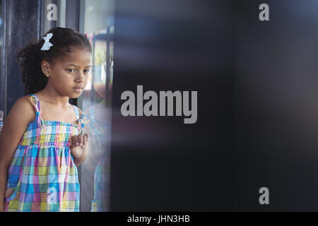 Thoughtful girl looking through window in school Stock Photo