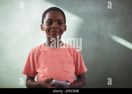 Portrait of smiling boy holding cellphone while standing against greenboard in school Stock Photo