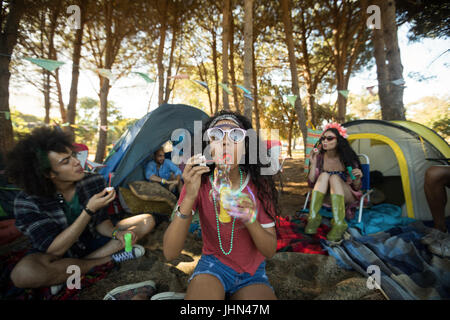Young woman blowing bubble wand with friends in background at campsite Stock Photo