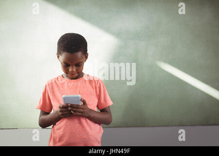 Boy using cellphone while standing against greenboard in school Stock Photo