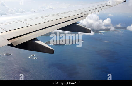 Part of an airplane wing with clouds, islands and the sea below. Stock Photo
