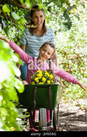 Girl enjoying with arms outstretched while smiling mother pushing wheelbarrow on footpath by plants Stock Photo