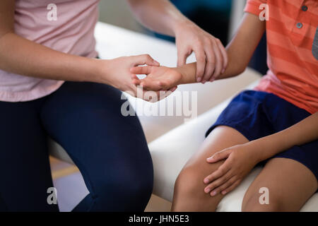 Midsection of female therapist examining wrist with boy sitting on bed at hospital ward Stock Photo