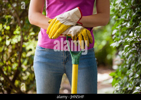 Midsection of woman holding gardening fork standing amidst plants at backyard Stock Photo