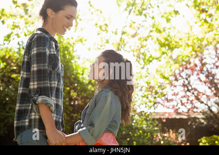 Smiling mother looking at daughter while holding her friends at backyard on sunny day Stock Photo