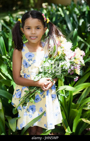 Portrait of smiling girl holding flowers bouquet standing amidst plants in backyard Stock Photo