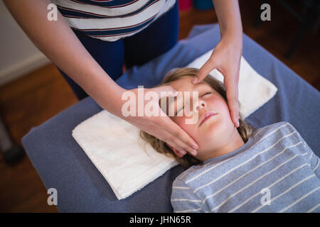 High angle view of boy with eyes closed receiving head massage from female physiotherapist at hospital ward Stock Photo