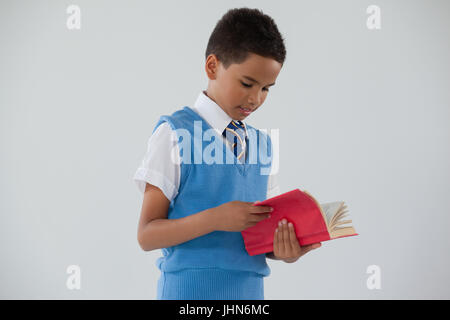 Attentive schoolboy reading book against white background Stock Photo