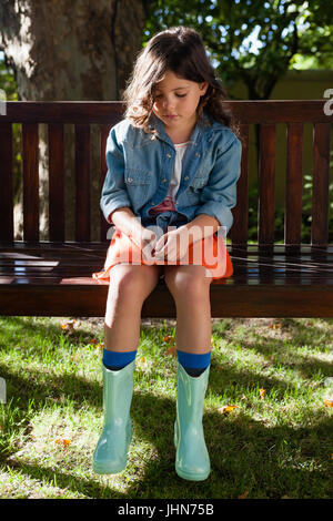 Upset girl sitting on wooden bench while looking down at garden Stock Photo
