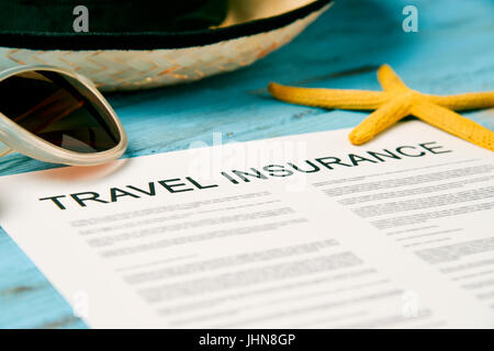 closeup of a travel insurance policy on a rustic blue wooden table, next to a pair of sunglasses, a straw hat and a starfish Stock Photo