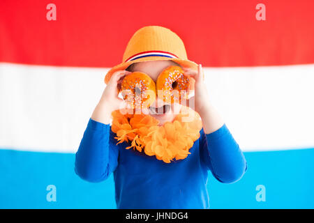 Little Dutch boy girl wearing country symbols eating orange donuts celebrating King day. Children support Holland sport team. Kids from the Netherland Stock Photo