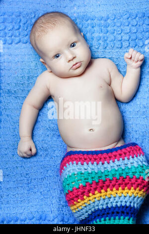 Child lies on a blue background. His legs were stuffed into a colored knitted cap Stock Photo