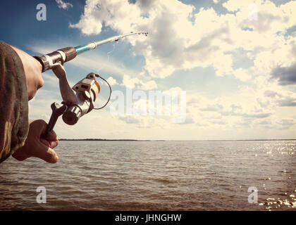 Close-shot of human hands holding a fishing-rod on the foreground Stock Photo