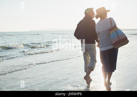 Barefoot mature couple walking on sunset beach Stock Photo