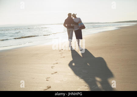 Affectionate mature couple hugging and walking on sunny beach Stock Photo
