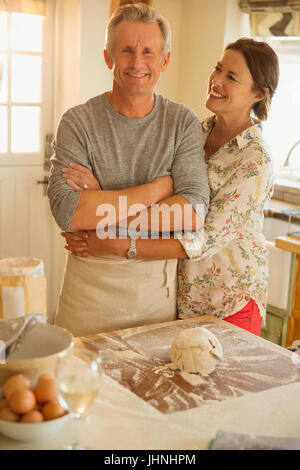 Smiling affectionate couple hugging, baking in kitchen Stock Photo